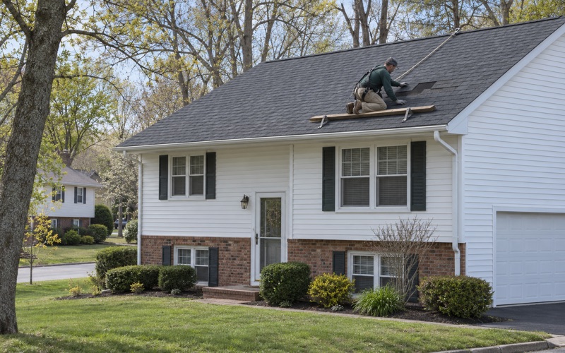 A roofer sliding a replacement shingle into a gap on the front slope of a Jackson Township bi-level.